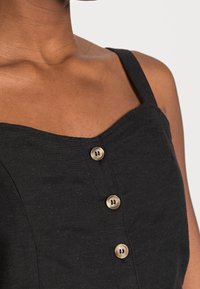 Top sans manches en lin noir avec un décolleté carré et trois boutons marron clair sur le devant. Texture lisse et coupe ajustée.