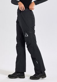 Schwarze Outdoor-Hosen mit schmaler Passform, hergestellt aus wasserabweisendem Stoff, verfügen über eine mit Reißverschluss verschlossene Tasche und ein Logo am Vorderbein.