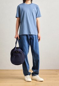 Světle modré bavlněné tričko s kulatým výstřihem, volné tmavě modré džínové kalhoty, bílé tenisky a kulatá námořnická taška z látky s držadlem.