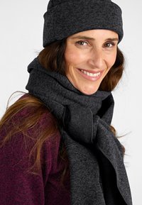 Gorro y bufanda de punto en gris oscuro, de grosor medio, con una textura suave. La bufanda cuenta con un acento anudado. El fondo es neutro.