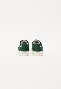 Grüne Leinensneaker mit niedrigem Profil, weißen Gummisohlen und dezenten Steppdetails. Die Rückansicht zeigt eine flache Ferse und den Kragen.
