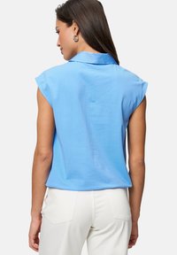 Blusa azzurro chiaro a maniche corte con colletto, realizzata in tessuto morbido, caratterizzata da un fit rilassato e una texture liscia.