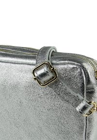 Silberfarbene Metalltasche mit strukturierter Oberfläche, versehen mit einer rechteckigen Schnalle in Goldoptik und einem Reißverschluss. Die Griffe sind durch abgesteppten Details hervorgehoben.