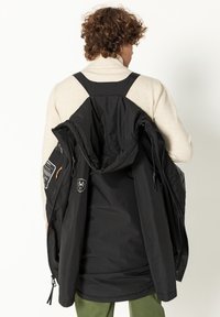 Zwarte geïsoleerde jas met een capuchon, verstelbare banden en een ontwerp met meerdere zakken. Kenmerken zijn contrasterende hardware en logo's. Lichtgewicht stof.