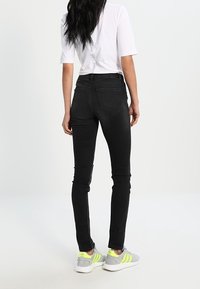 Jeans negros ajustados con cintura alta y dos bolsillos traseros, combinados con una camiseta blanca de manga corta y zapatillas grises con detalles en neón.