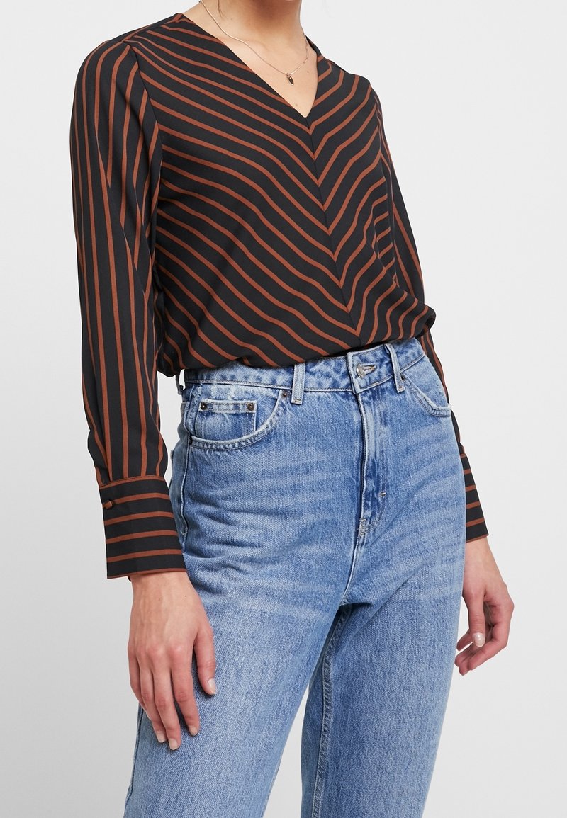 Blusa negra de manga larga con rayas diagonales en color óxido, diseño de cuello en V, combinada con jeans de denim claros de tiro alto.