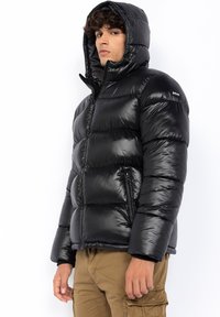 Doudoune noire avec une finition brillante, capuche et poches zippées ; dotée d'un design matelassé et de fermetures éclair robustes.