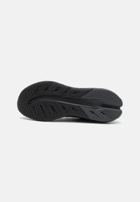 Semelle de chaussure de sport noire dotée d'un motif texturé, de rainures pour l'adhérence et d'ouvertures pour la flexibilité. Fabriquée en matériau synthétique durable.