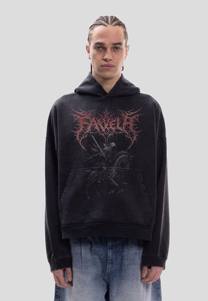 Junge Person mit Zöpfen trägt schwarzen Hoodie mit rotem, filigranem Text und einer Grafik eines dunklen Ritters zu Pferd, kombiniert mit ausgebleichten blauen Jeans.