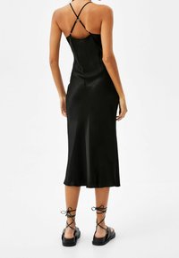 Svart satin klänning med halvlång fåll, med tunna justerbara axelremmar och rak rygg. Kombinerad med svarta snörsandaler.