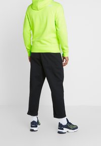 Neongrön huvtröja med en svart logotyp, kombinerad med svarta byxor. Vita strumpor och marinblå sneakers med gröna detaljer fulländar outfiten.