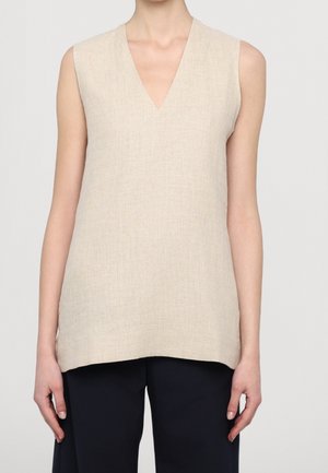 Top de lino sin mangas en color beige con escote en V, combinado con pantalones negros, vestido por una persona de pie frente a un fondo claro y liso.