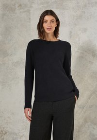 Marineblau gestrickter Pullover mit Rundhalsausschnitt, langen Ärmeln und einer strukturierten Musterung. Kombiniert mit dunkelgrauen Hosen.