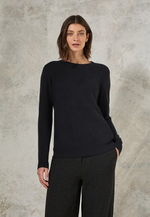 Pull en maille bleu marine avec un col rond, des manches longues et un motif texturé. Assorti avec un pantalon gris foncé.