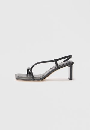 Sandale noire à lanières avec un bout carré et un talon carré. Elle présente des fines lanières métalliques et une semelle en cuir lisse. Design minimaliste.