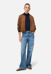 Hnědá bomber bunda z broušené kůže, námořnicky modrý top, světle modré rozšířené džíny, béžové boty z broušené kůže. Jednoduchý design, volný střih, bez viditelných vzorů nebo kovových prvků.