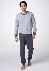 Felpa grigia e pantaloni della tuta grigio scuro, entrambi in tessuto morbido. La felpa presenta uno scollo a contrasto e una piccola grafica di montagna.