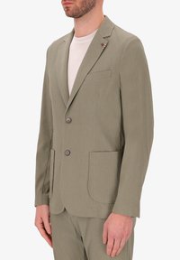 Blazer verde chiaro con texture, due bottoni, rever a punte e due tasche anteriori. Un piccolo dettaglio a spilla è accentuato sul rever.