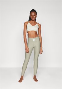 Sostén deportivo verde claro con tirantes finos, combinado con leggings de cintura alta a juego, ambos con una textura suave y acanalada y acentos de logo.