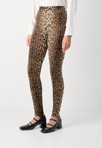 Leggins z vzorcem leoparda v rjavi in črni barvi, z elastičnim pasom in oprijetim krojem, v kombinaciji s črnimi čevlji na blok peti.