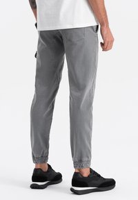 Grijze tapered broek met elastische manchetten, gemaakt van lichtgewicht stof. Gecombineerd met zwarte sneakers met een gestructureerde bovenkant en een witte zool.