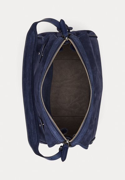 Tamsiai mėlynos spalvos zomšinė rankinė su užtrauktuku, tamsia vidine dalimi ir reguliuojamu dirželiu. Turi lygią tekstūrą ir blizgančius sidabrinius metalinius akcentus.