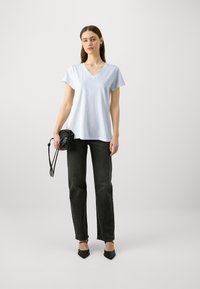 Lyseblå V-hals t-shirt i bomuldsblanding, parret med højlinjede sorte jeans og sorte spidse sko. Holder en lille sort taske.