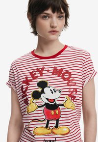 Rød og hvid stribet t-shirt med rund hals, der har et grafisk motiv af Mickey Mouse i sort, rød og gul. Blødt stof, korte ærmer.