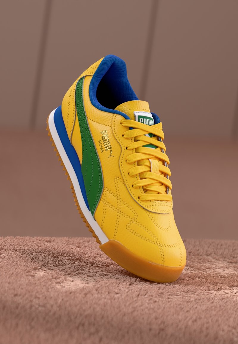 Baskets en cuir jaune avec des accents verts et bleus, surface texturée, design à lacets, semelle blanche et marquage doré sur le côté.