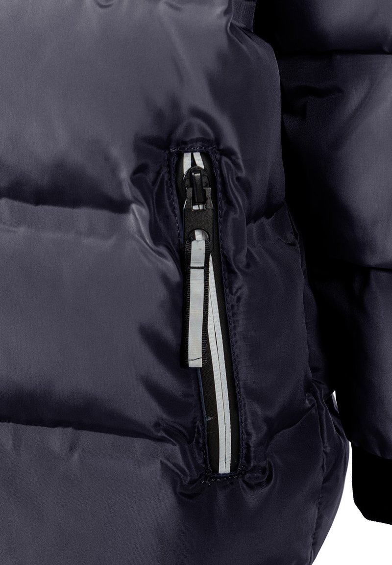Giubbotto imbottito navy con texture lucida e trapuntata. Presenta una tasca con zip sul lato sinistro con hardware nero e accenti bianchi.