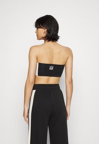 Čierno-biely bezramienkový top s elastickým pásom a logom na chrbte; model má na sebe čierne široké nohavice so bočnými prúžkami.