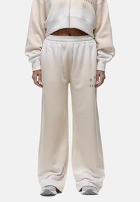 Crème-kleurige sweatpants gemaakt van zacht materiaal met een elastische tailleband, ruime benen en subtiele bedrukte accenten aan de zijkant.