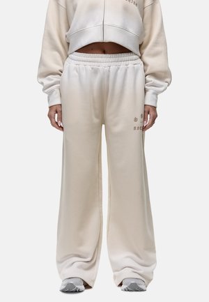 Crème-kleurige sweatpants gemaakt van zacht materiaal met een elastische tailleband, ruime benen en subtiele bedrukte accenten aan de zijkant.