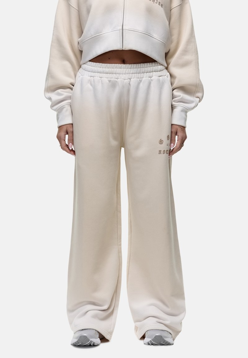 Crème-kleurige sweatpants gemaakt van zacht materiaal met een elastische tailleband, ruime benen en subtiele bedrukte accenten aan de zijkant.
