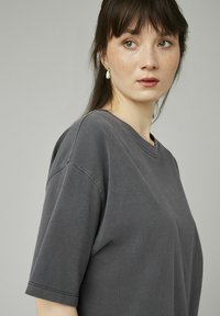 T-shirt oversize gris charbon à manches courtes, avec un col rond classique et une texture douce et lisse. Design simple et sans caractéristiques.