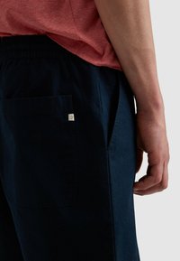 Die marineblauen Jogginghosen haben einen elastischen Bund und Seitentaschen. Der Stoff hat eine weiche Textur und ein kleines Logoshirt befindet sich in der Nähe der Gesäßtasche.