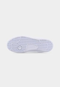 Semelle d'une sneaker blanche Lacoste avec motif de bande de roulement en grille et détail de grip circulaire sur un fond clair uni.