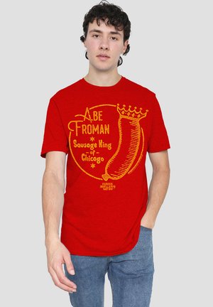 Red T-shirt featuring a yellow graphic with text "Abe Froman Sausage King of Chicago" and a sausage icon, short sleeves, crew neck design.