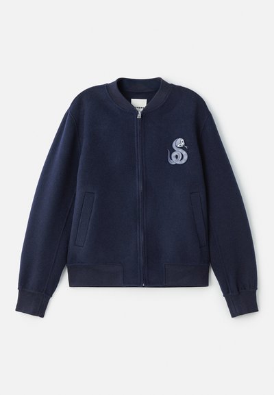 Jūrinis zip-up bombonešis, pagamintas iš minkštos medžiagos, su nedideliu gyvatės siuvinėjimu kairėje krūtinės pusėje ir dviem šoninėmis kišenėmis.