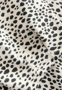 Tejido de algodón con una base crema y manchas de leopardo negro dispersas; textura suave con tamaños de manchas variables. Costura visible.