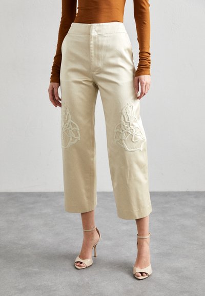 Pantaloni bej scurți cu broderie texturată albă în față, design cu talie înaltă, fabricați dintr-un amestec de bumbac, asortați cu tocuri nude.