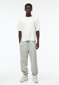 Witte, korte mouwen t-shirt gecombineerd met lichtgrijze joggers. De joggers hebben een elastische tailleband en strakke boorden, aangevuld met witte sneakers.