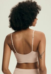 Miękki beżowy biustonosz braletka z regulowanymi ramiączkami, bezszwowa konstrukcja i gładka faktura. Posiada szeroki pasek i nisko wycięty tył.