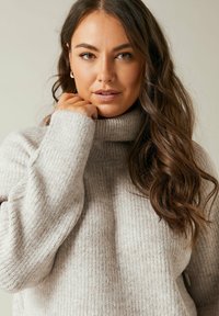 Maglione a collo alto rigato di colore grigio chiaro con superficie testurizzata. Presenta maniche lunghe e un collo alto, creando un aspetto accogliente.