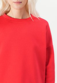 Sudadera roja hecha de una tela suave. Presenta un cuello redondo, mangas raglán y una textura lisa con detalles de costura mínimos.