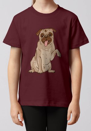 Kind trägt ein kastanienbraunes T-Shirt mit einer Illustration eines lächelnden Mops, der eine Pfote vorne hebt.