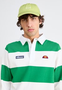 Grün-weiß gestreiftes Polohemd mit Kragen, das ein gesticktes 'ellesse'-Logo sowie ein kleines farbiges Logo auf der Brust aufweist. Hellgrüne Mütze mit "HUF"-Text.