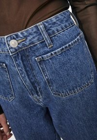 Jeans in denim di un blu medio con un classico design a cinque tasche, caratterizzati da cuciture visibili, una chiusura a bottone in metallo e una vestibilità leggermente rilassata.