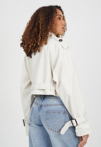 Krótką białą kurtkę z wysokim kołnierzem, dużymi guzikami i regulowanymi paskami przy rękawach połączono z jasnoniebieskimi dżinsami.