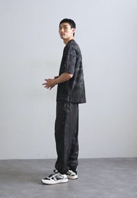 Camiseta gráfica negra de manga corta, combinada con pantalones de chándal negros. El calzado presenta acentos en blanco y negro, creando un look deportivo.